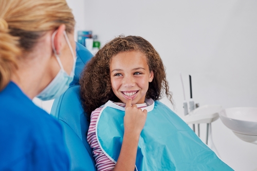 Smiling,Girl,Pointing,To,Tooth,While,Sitting,In,Dental,Chair.